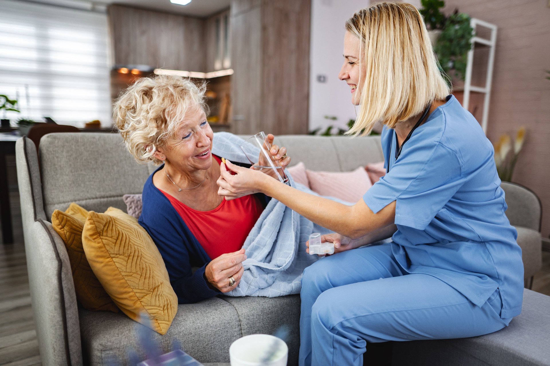 Nurse assisting senior woman taking medicine on sofa at home